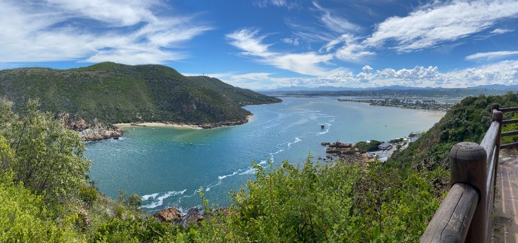 The Knysna Heads from a high viewpoint: two green headlands, a turquoise channel, and the lagoon opening toward distant mountains.