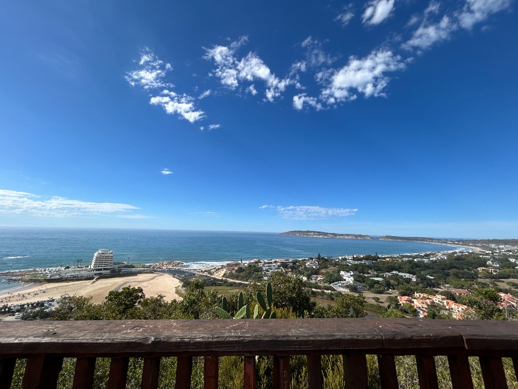 Plettenberg Bay from a wooden lookout: Beacon Island on the left, a wide beach, and Robberg stretching into a blue bay.